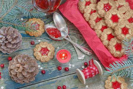 甜的圣诞饼干红果酱鲜树枝和锥红莓果烧蜡烛和在旧木制桌子上带装饰丝的波宾饼图片