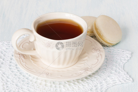 一杯古老的黑茶和两杯红马卡松蛋糕放在白的自制拉西餐巾纸上图片