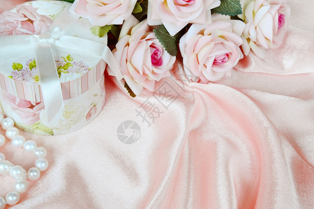 粉红玫瑰圆礼盒和丝织物上的珍珠项链图片