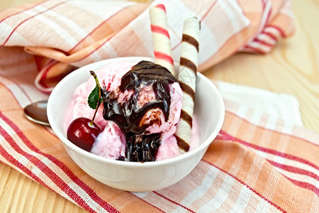 碗中的冰淇淋樱桃巧克力糖浆和面包卷在木板背景的餐巾纸上图片