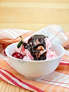 碗中的冰淇淋樱桃红餐巾纸上的巧克力糖浆在木板背景上图片