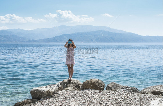 女人在海滩上用智能手机拍照图片