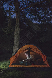 男人晚上在帐篷里看他的智能手机图片
