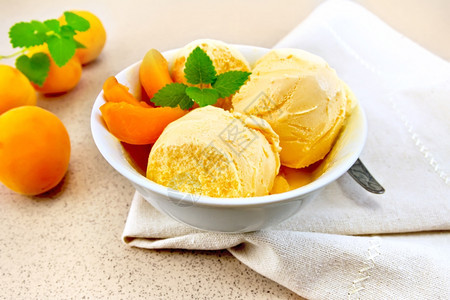 白碗中的杏仁冰淇淋里面有水果片餐巾纸上的薄荷在背景花岗岩桌上图片