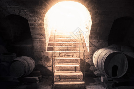 明亮的光束从一个古老的酒窖入口下来启发了石头楼梯和旧木桶图片