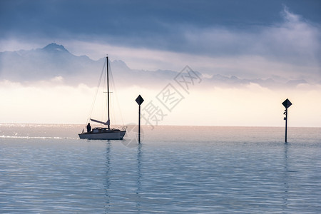 在港湾湖和山岳上划着一条船浮云在地平线上晨光下图片