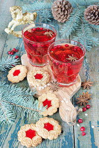 圣诞节桌两杯红热辣味葡萄酒配香料和牛莓果酱的饼干围着圆形树枝和锥图片