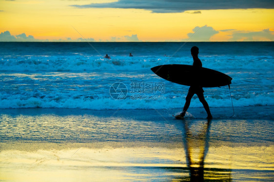 日落时在海边散步的冲浪者图片