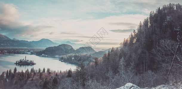 日出时冬季全景湖水和村庄流血周围环绕着朱廉阿尔卑斯山和安装在三脚架上的照相机图片