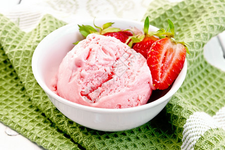 白碗中的冰淇淋草莓绿色餐巾纸上的浆果在木板背景上图片