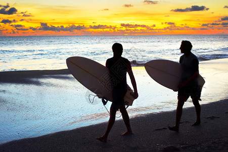 日落时在海滨散步的两名冲浪者在板上行走图片