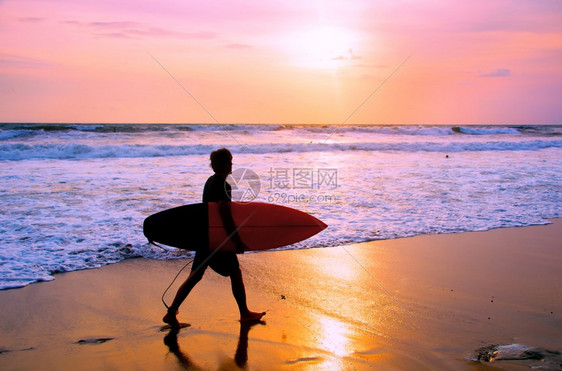 日落时在沙滩上走着冲浪板图片