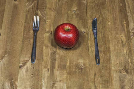 木板表面躺着一把刀叉子和红苹果图片