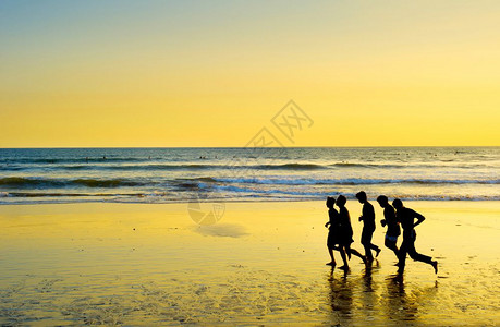 日落时在海滩上奔跑的一群男人图片