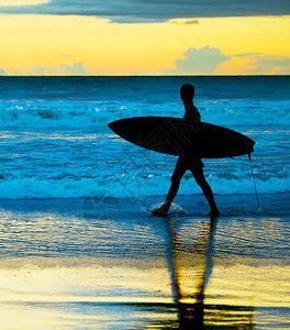 日落时在海边散步的冲浪者图片