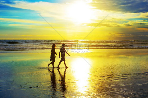 日落时在海滩上散步的情侣图片