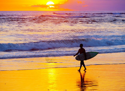 日落时在海滩上走着冲浪板者图片