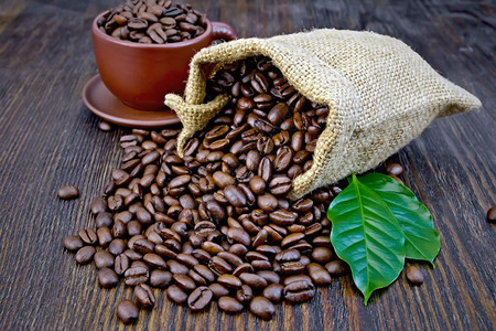 黑咖啡豆棕杯和木板背景的绿叶图片