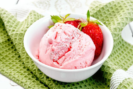 白碗中的冰淇淋草莓和浆果在绿色餐巾纸上与浅木板对着图片