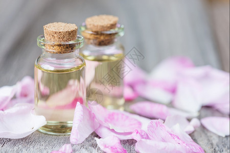 两瓶精油和粉红玫瑰花瓣放在桌上图片
