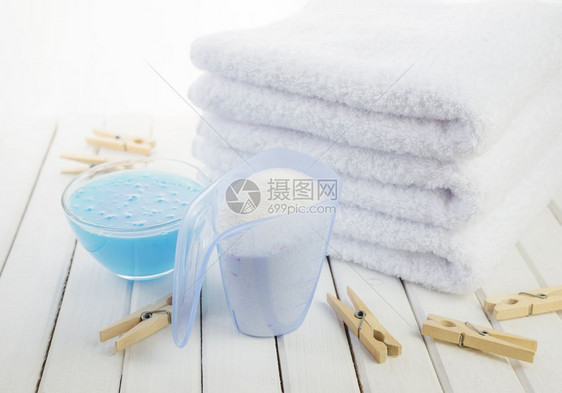 3条白色毛浴巾测量杯中的洗衣粉透明玻璃碗中的蓝织布软体和白板底的木制衣图片