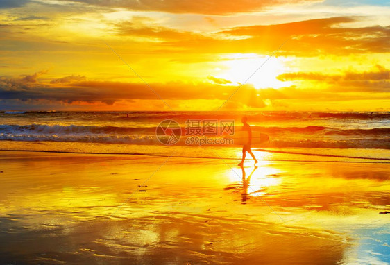 日落时在海滩上与冲浪板散步的者图片