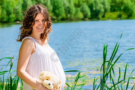 可爱的怀孕女孩在公园中美丽的湖底背景在公园装扮图片