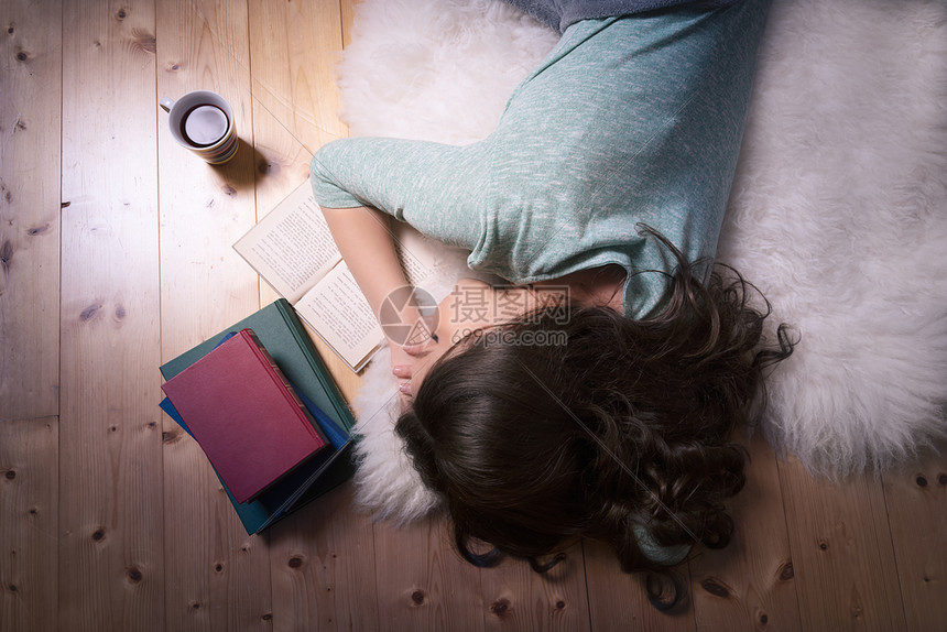 与一个年轻的黑发女孩睡着看一本书躺在白毛上直接躺在地板上图片