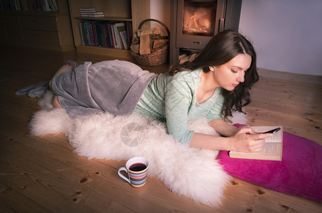 黑发女孩在壁炉前躺在白毛毯上放松同时使用智能手机查阅资料图片