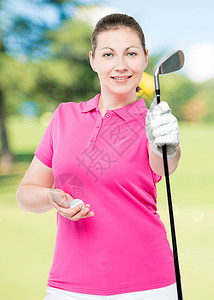 在高尔夫球场背景上握着棍棒和球的女高尔夫手图片