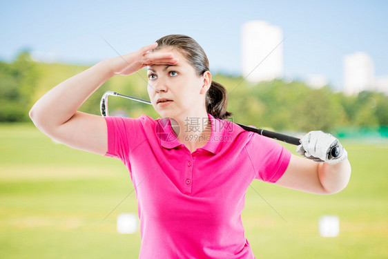穿着粉红色T恤与高尔夫俱乐部看着距离在高尔夫球场的背景图片