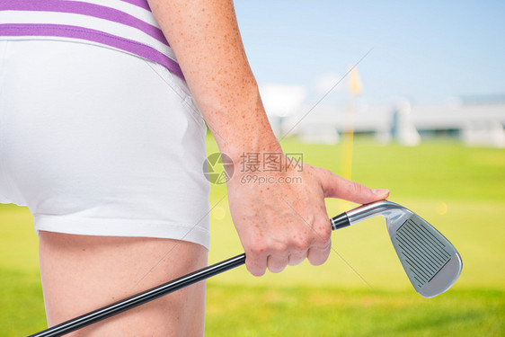 一个高尔夫俱乐部在一个年轻的女运动员手里关闭高尔夫球场的背景图片