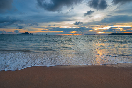 美丽的海浪和沙滩在地平线上太阳在山落下图片
