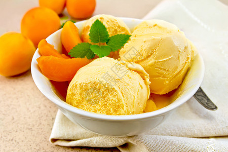 白碗中的杏子冰淇淋配有水果片餐巾上的勺子放在背景花岗岩桌上图片