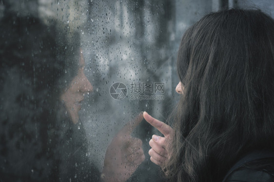 黑褐色年轻女人和她对窗户的反光满是雨滴图片