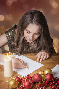 美丽的年轻女孩在烛光时写给圣达克萨斯周围都是多彩的球体和其他圣诞装饰图片