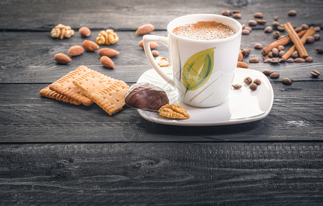 盘子上的热咖啡杯周围是美味健康的零食饼干杏仁核桃和咖啡豆图片