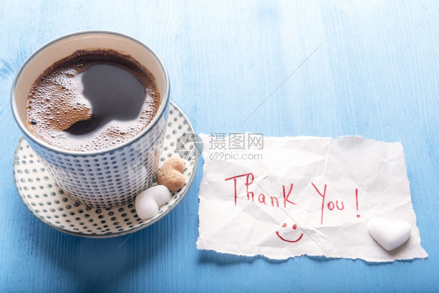 纸条上写着感谢信息微笑的面孔一杯热辣的芳香咖啡里面有心形糖放在蓝木桌上阳光明媚的一天图片