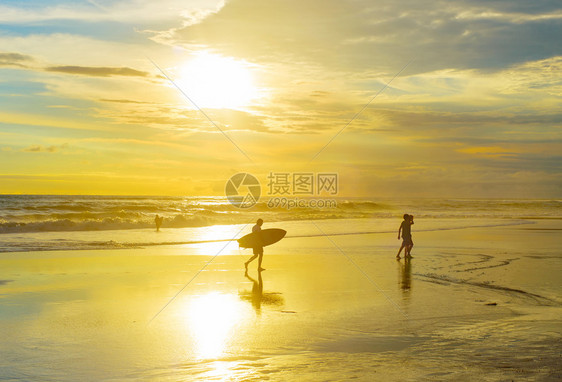 日落时在海滩上与冲浪板散步的者图片