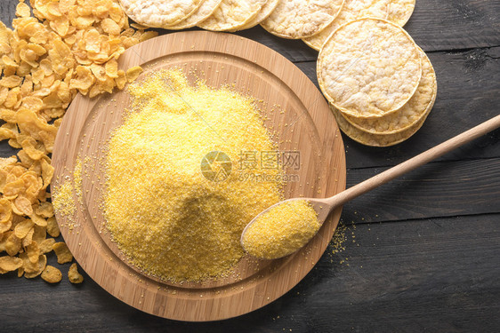 圆木板上装满玉米面粉的圆木板四周环绕着黑木桌上的面粉玉米片和饼图片