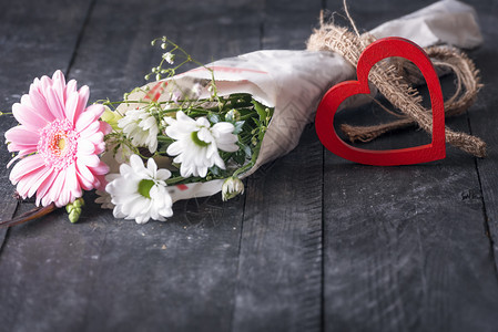 贺卡设计上有一束可爱的花包在报纸上的花朵和装饰木心挂在旧黑桌子上图片
