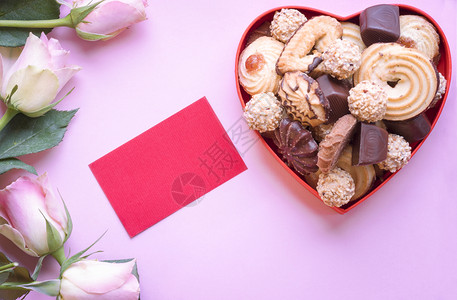 充满美味饼干和巧克力的心形盒可爱粉红玫瑰和一张空纸图片