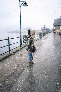 身穿厚外套的年轻女子身着寒冷的天气站在雪地下看着大厅见湖在天堂奥斯特里亚图片