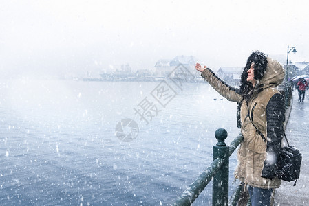 冬天年轻女性站在湖边用手接雪图片