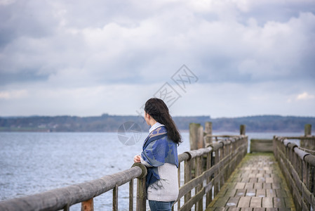 年轻女子独自站在老木桥上思考和凝视着下午的地平线在墨西哥湖上巴伐利亚德国图片