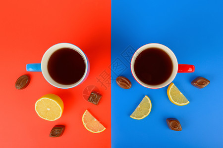红色和蓝杯子有茶柠檬片和巧克力糖果放在红色和蓝背景上平坦的躺地顶楼空闲的文本间图片