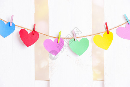 爱的概念不同彩色纸心绑在一根绳子上木质多色夹子和白木栅栏在背景图片