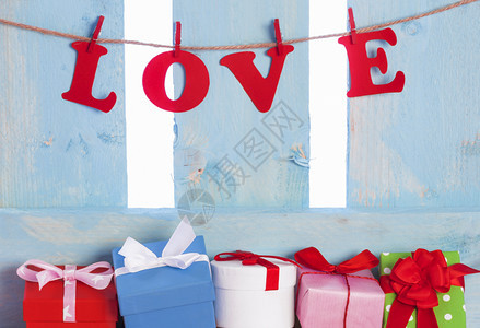 在蓝色木栅栏下充满多彩的礼物和用红色纸字拼写的爱绑在带木片的绳子上图片