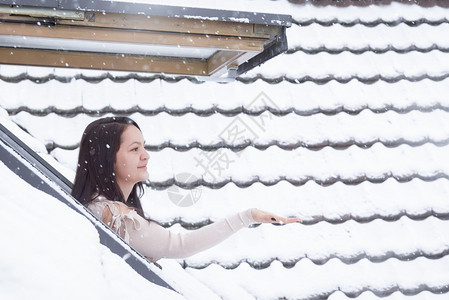 年轻美女站在窗口前用手接落下的雪花图片