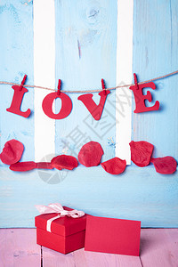 可爱的红色礼物盒上面有一张空白的留言卡上面写着爱的红纸信挂在一根绳子上蓝木篱笆图片